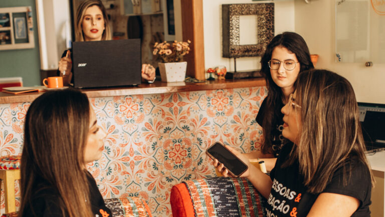 Equipe de mulheres conversando em um ambiente descontraído de trabalho, com foco na colaboração e comunicação, representando processos de gestão de pessoas.