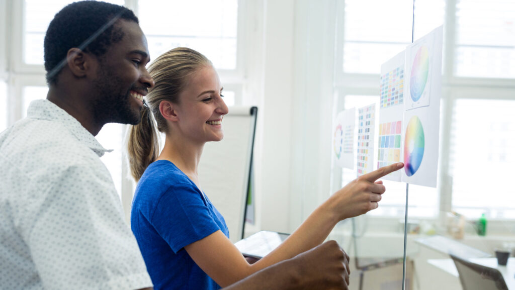 Colaboradores sorridentes discutindo gráficos e tabelas fixadas em um quadro transparente, durante o processo de onboarding em uma empresa de tecnologia.